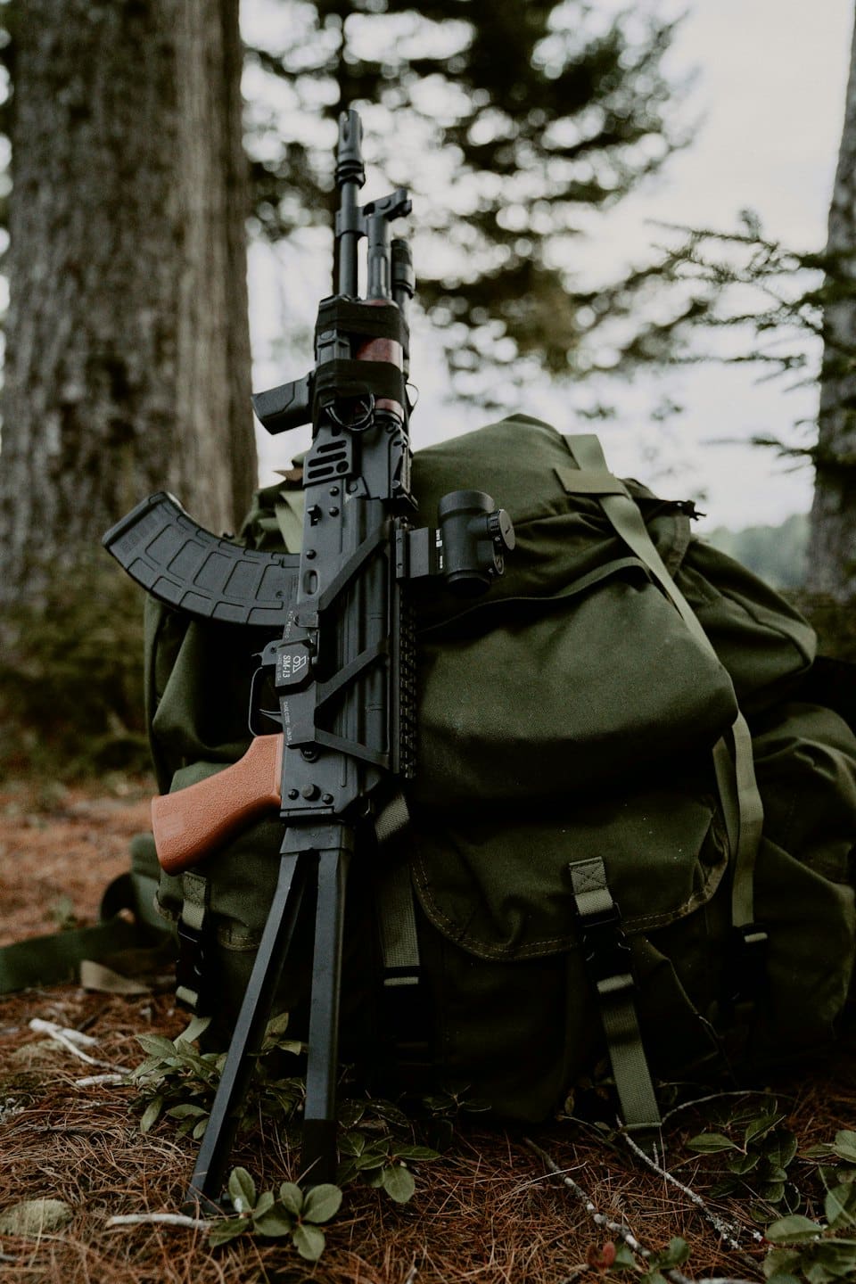 Fucile tattico con impugnatura in legno appoggiato a uno zaino militare.
