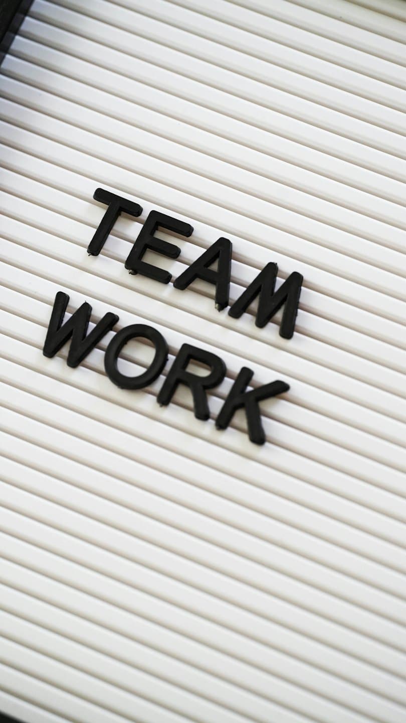 Lettere tridimensionali nere compongono la scritta 'TEAM WORK' su una bacheca scanalata.
